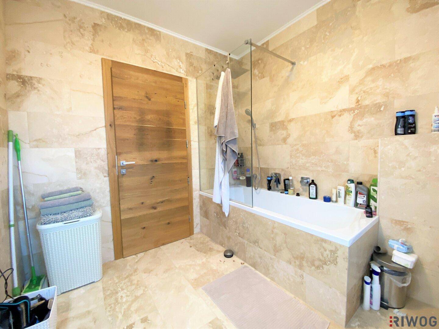 Geräumiges Badezimmer mit Badewanne, Duschbereich und beigefarbenen Natursteinfliesen.