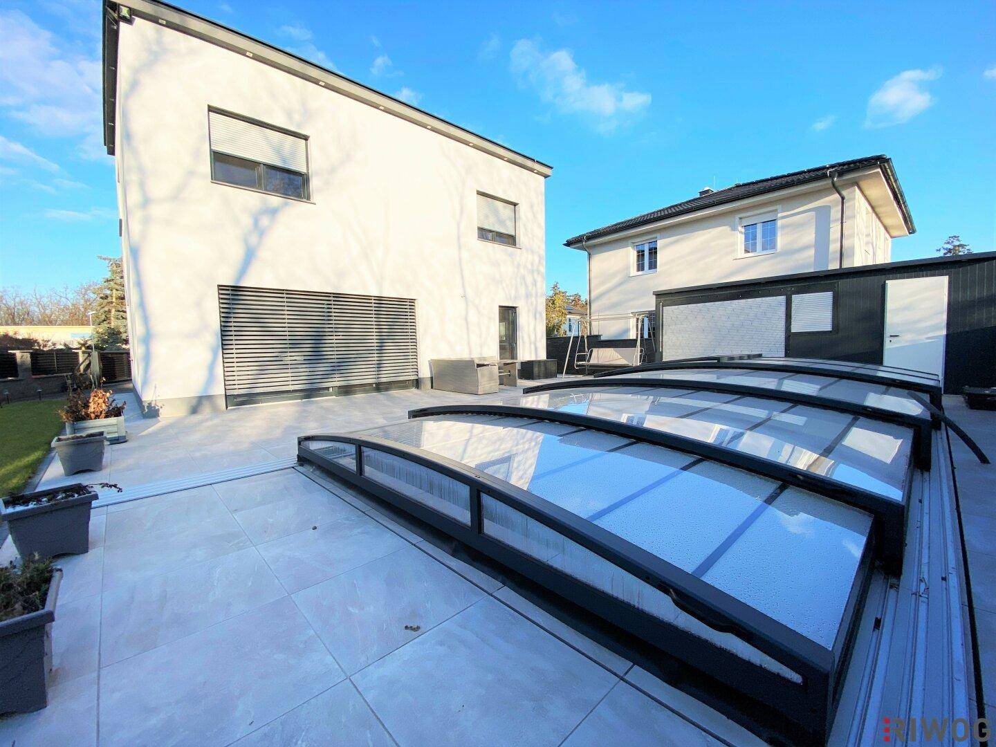 Moderne Terrasse mit Fliesenboden und überdachtem Poolbereich hinter dem Haus.
