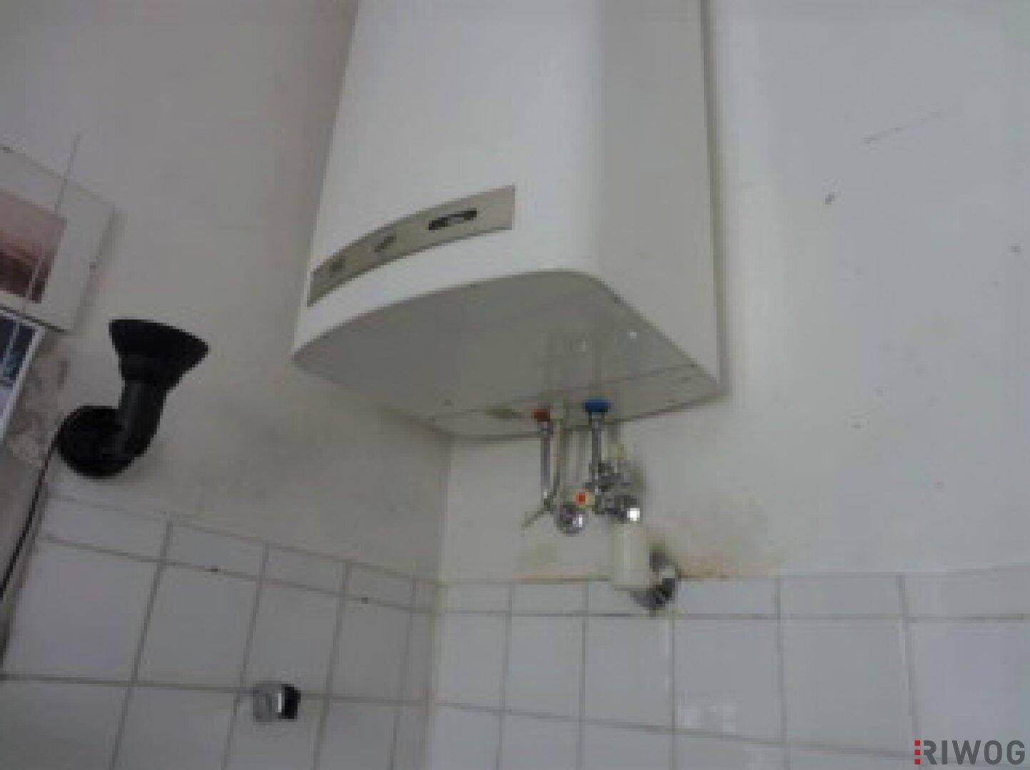 Wandmontierter Warmwasserbereiter in einem Badezimmer mit weißen Fliesen.