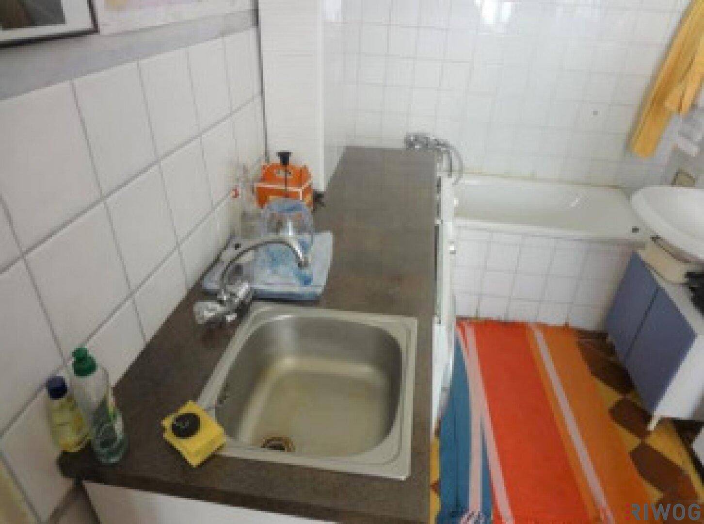 Kleine Küchenzeile mit Spülbecken, Arbeitsplatte und bunten Teppichen.