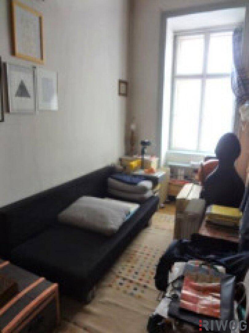 Kleines Zimmer mit Sofa, Fenster und Holzboden.