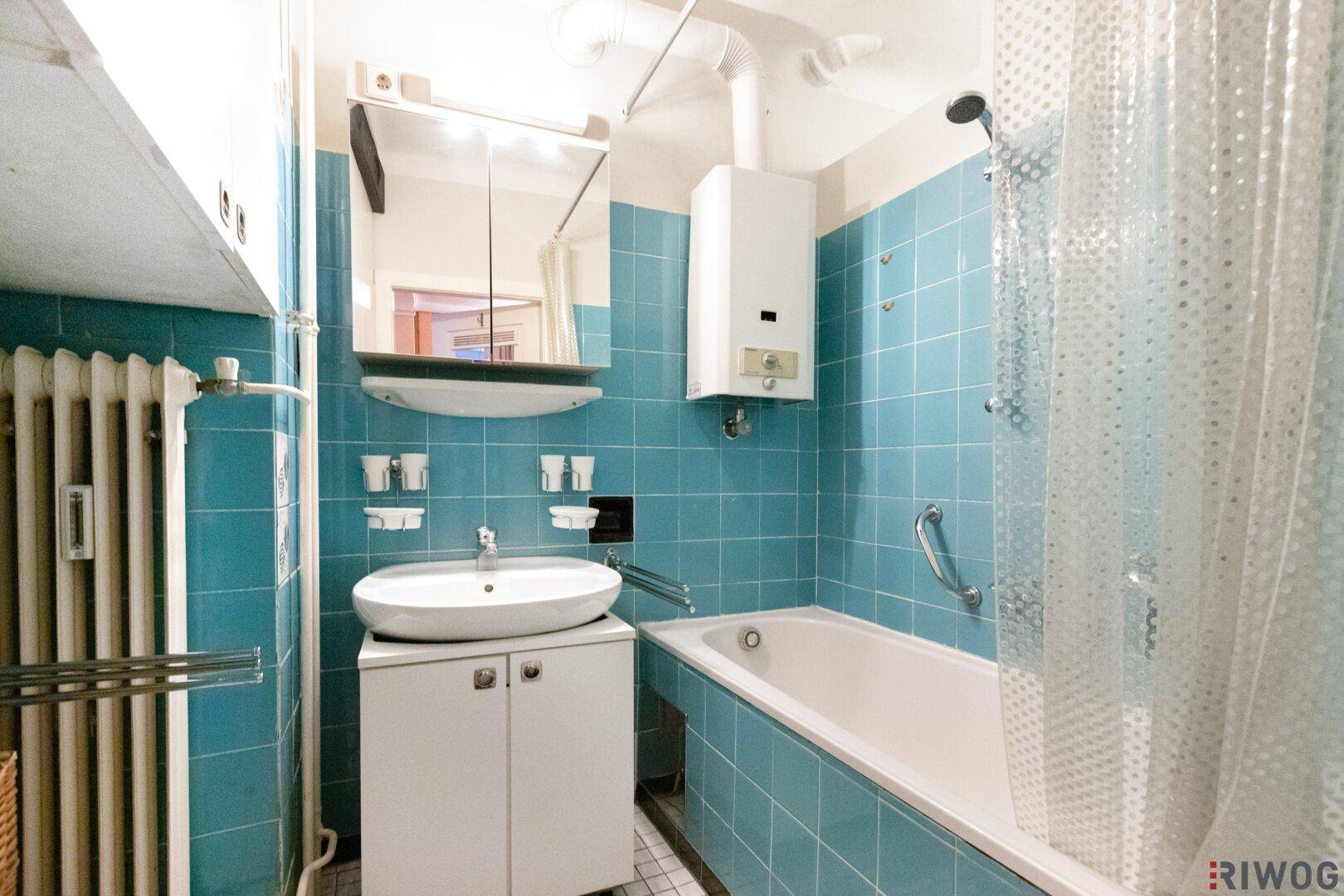 Badezimmer mit blauen Fliesen, Badewanne mit Duschfunktion und Waschtisch.