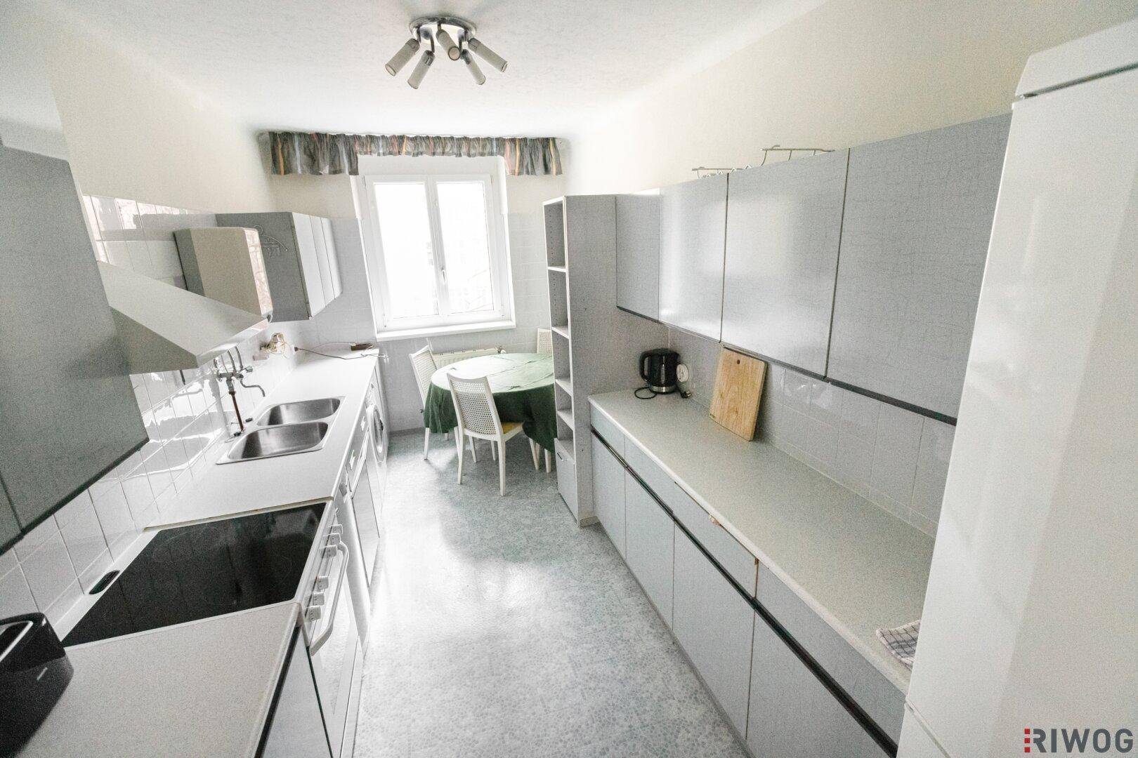 Funktionale Küche mit grauen Schränken, Essbereich und Fenster für Tageslicht.