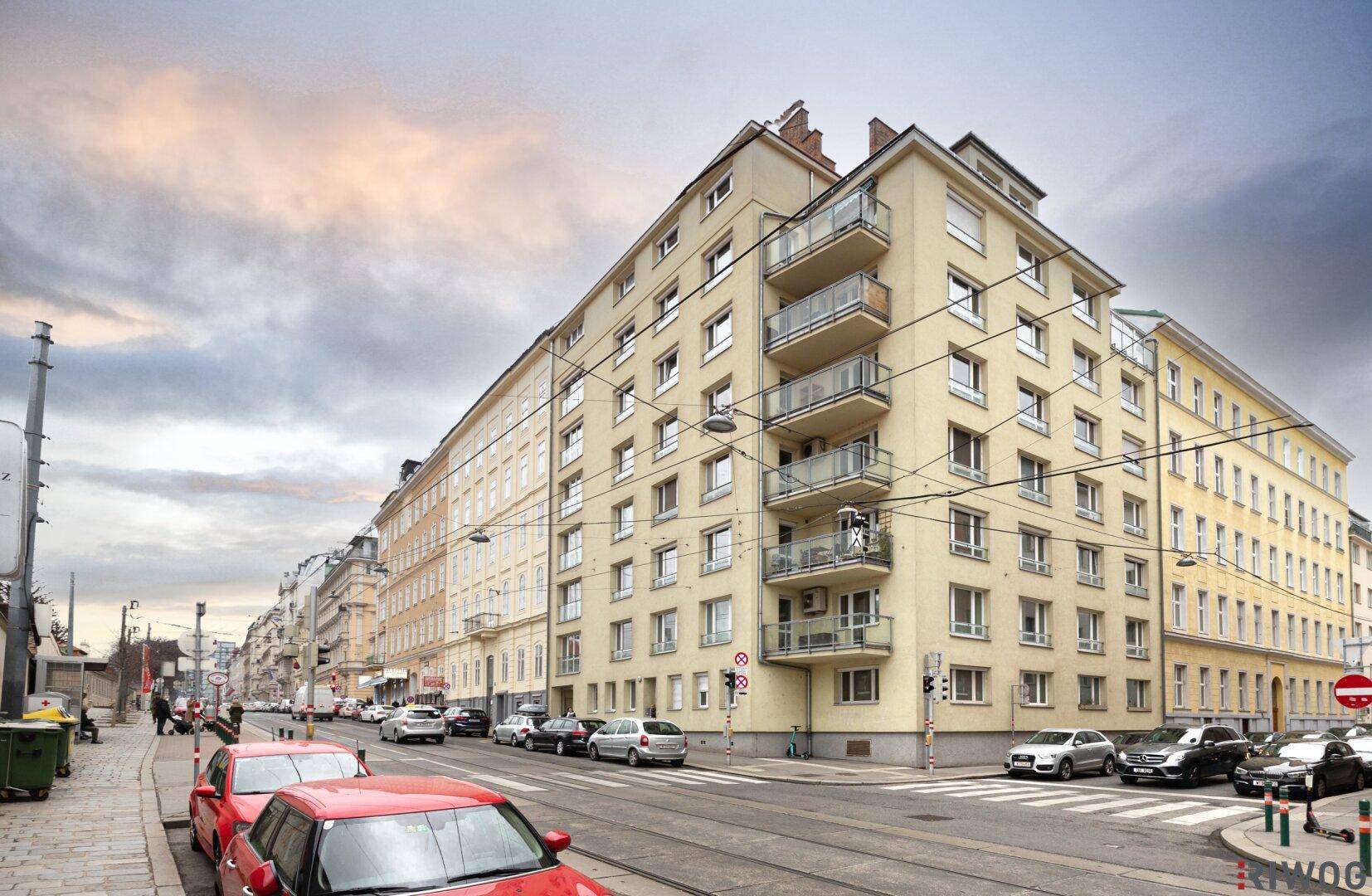 Historisches Wohngebäude an einer belebten Straße mit Balkonen und vielen Fenstern.