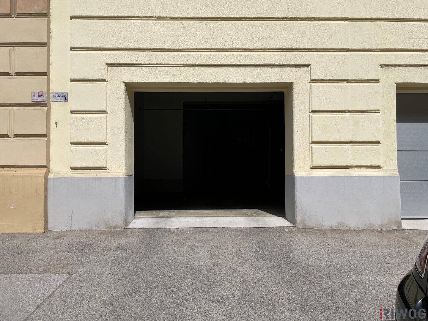 Eingang zur Tiefgarage eines Gebäudes mit klassischer Fassade und grauen Akzenten an einem sonnigen Tag.
