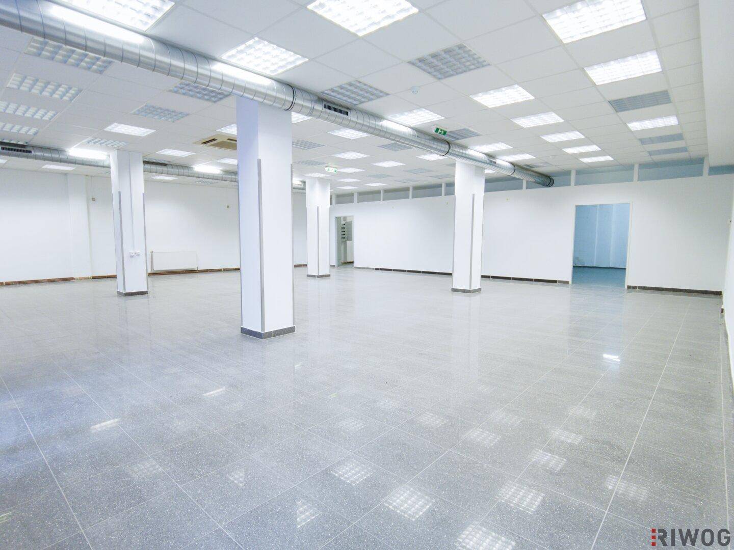 Großer, offener Gewerberaum mit Säulen, Fliesenboden und sichtbaren Lüftungsrohren an der Decke.