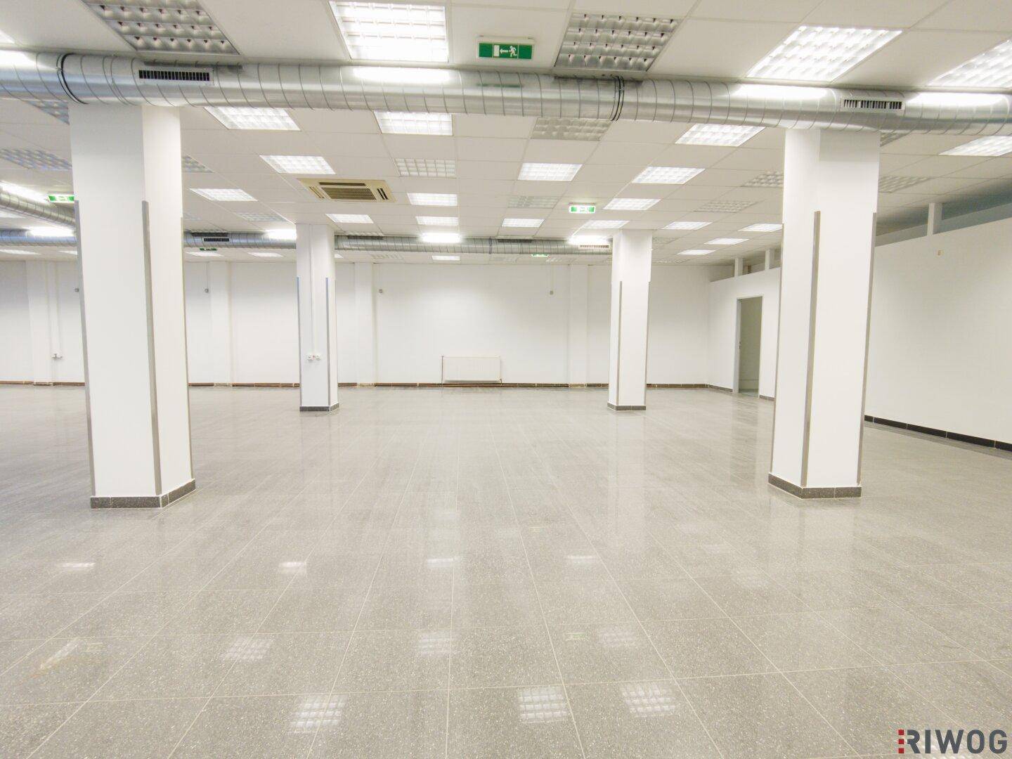 Weitläufiger Gewerberaum mit Säulen, Fliesenboden und einer Decke mit vielen integrierten Leuchten.