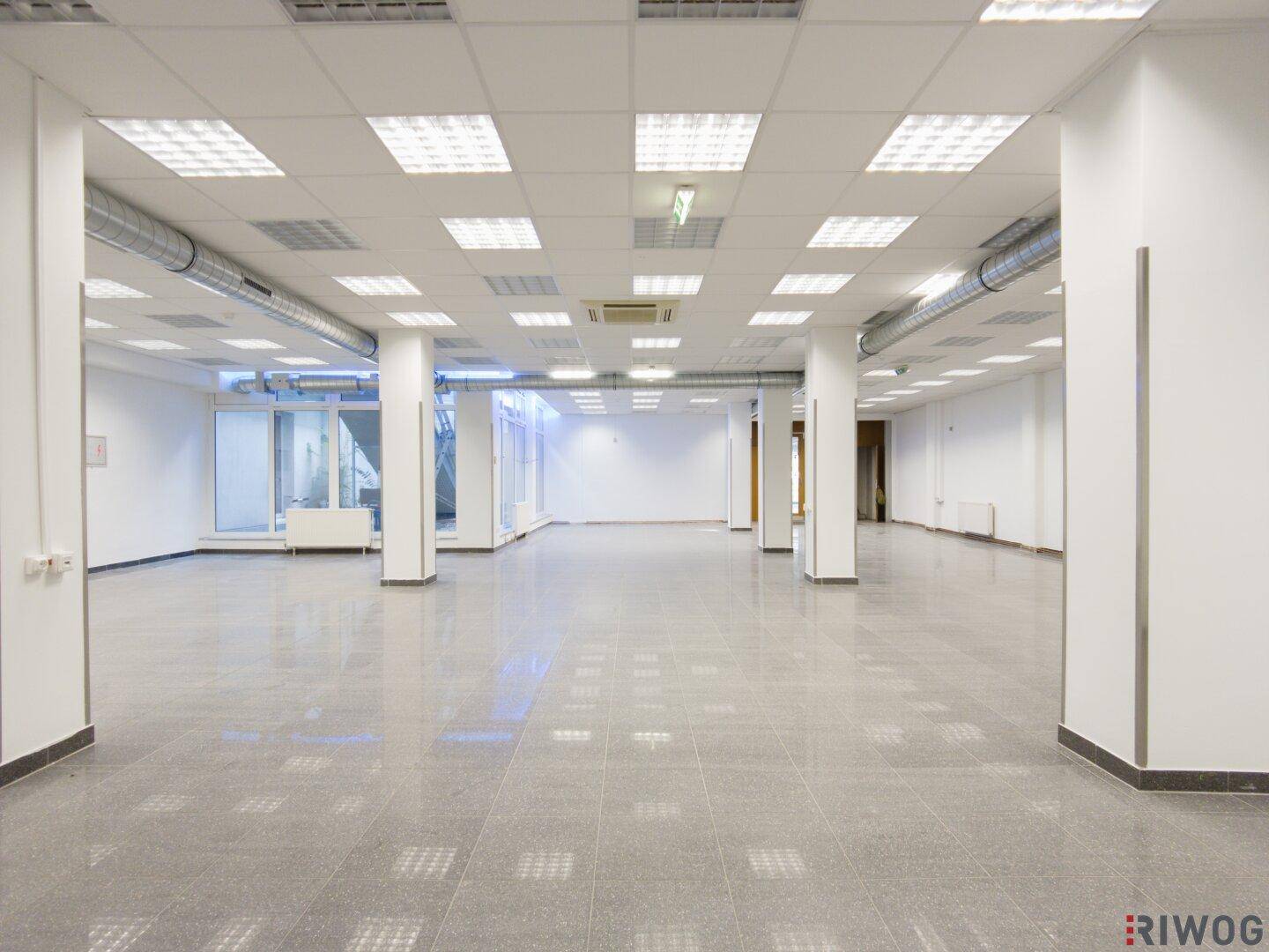 Heller, offener Gewerberaum mit Säulen, glänzenden Fliesen und einer Glasfront im Hintergrund.