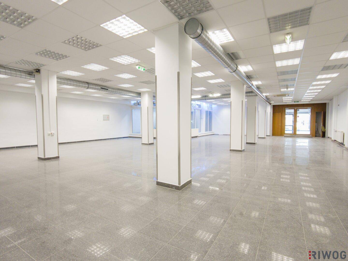Geräumiger Gewerberaum mit Säulen, Fliesenboden und einer Decke mit vielen integrierten Leuchten.