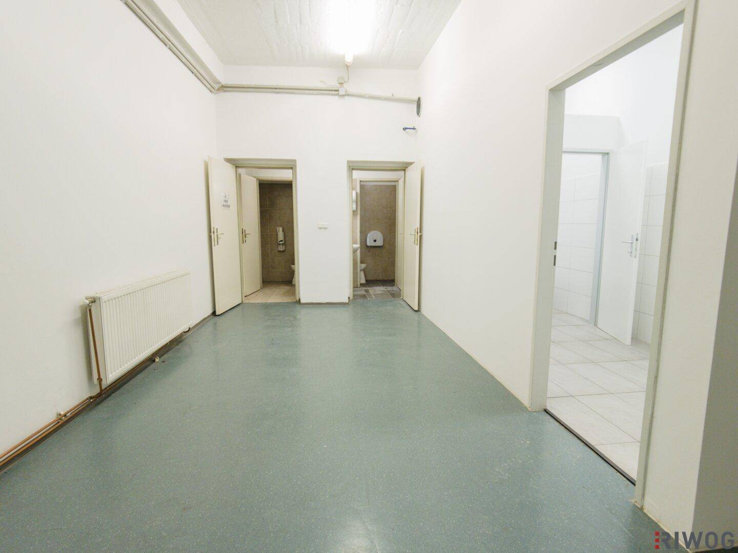 Heller Flur mit hellblauer Bodenbeschichtung, weißen Wänden und Zugang zu mehreren Toilettenräumen.