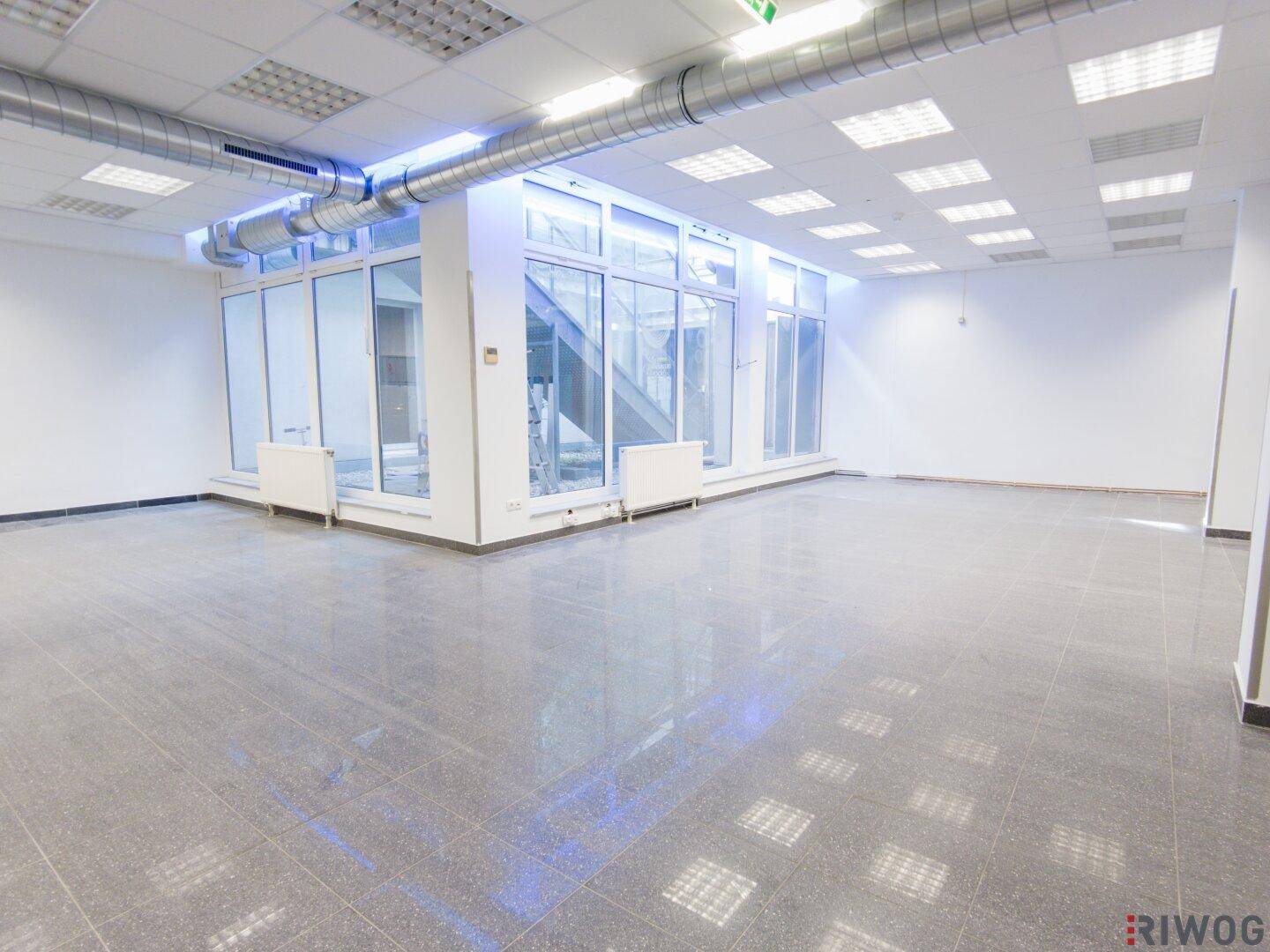 Großer, heller Gewerberaum mit glänzenden Fliesen, Säulen und einer markanten Glasfront.
