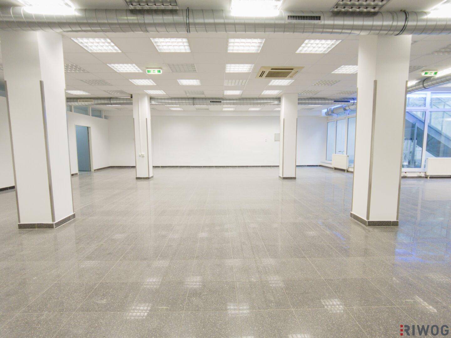 Weitläufiger Gewerberaum mit Säulen, Fliesenboden und einer Decke mit vielen integrierten Leuchten.