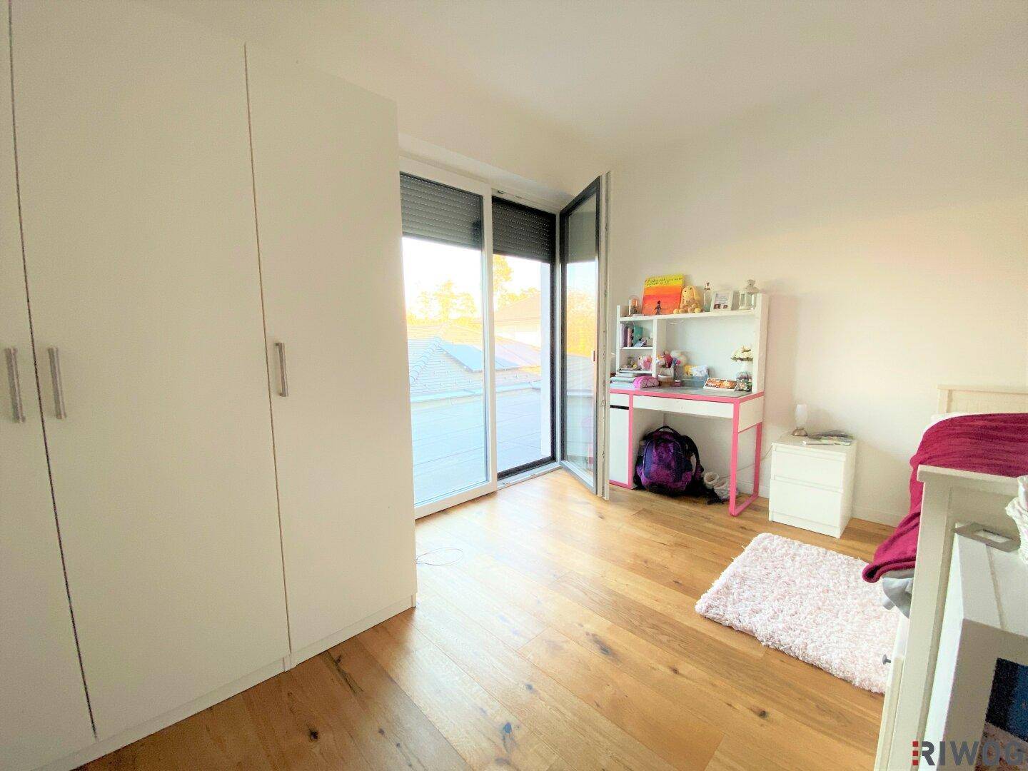 Helles Schlafzimmer mit Holzboden, Kleiderschrank und Zugang zu einem Außenbereich.