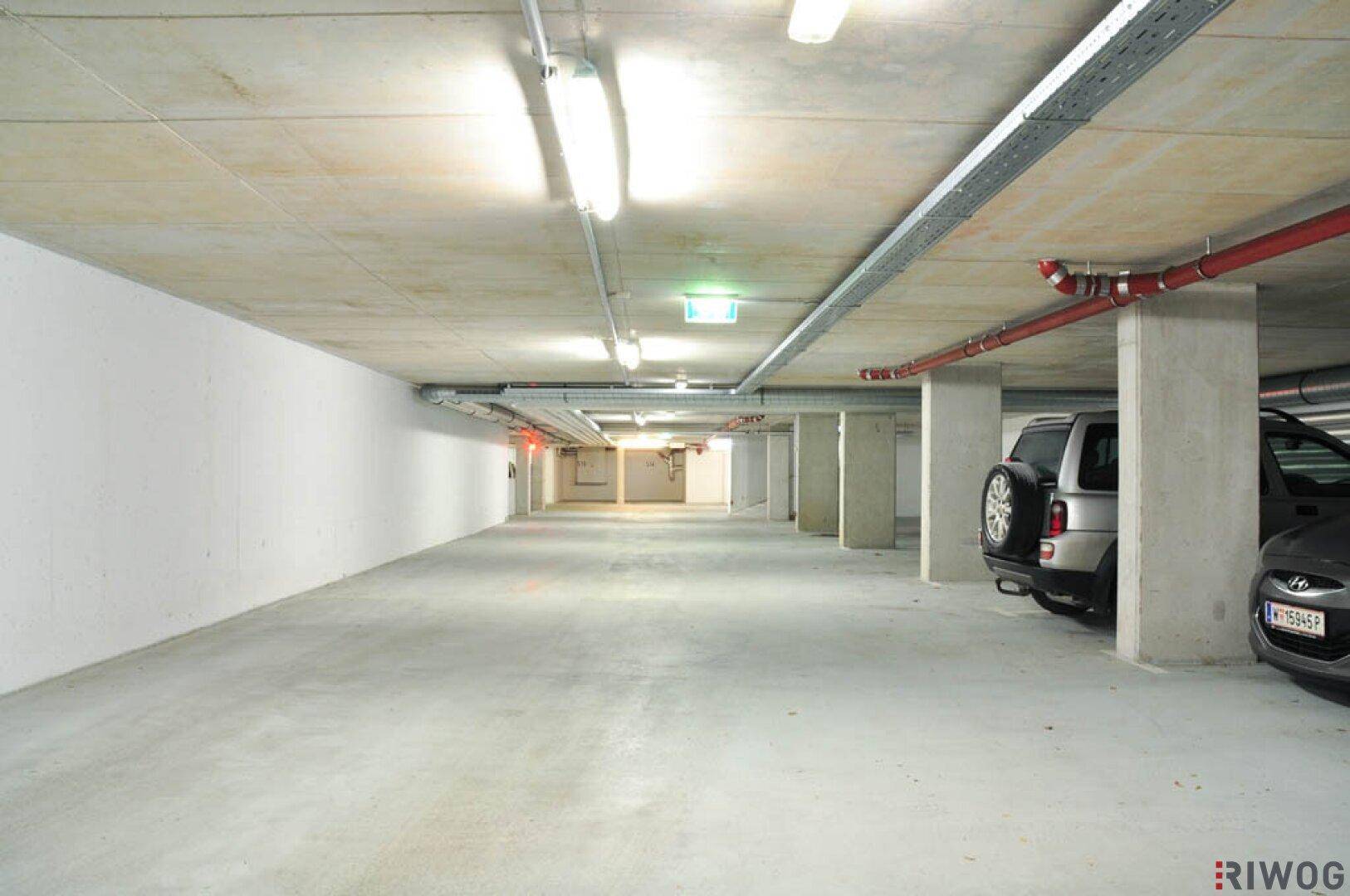Helle Tiefgarage mit mehreren Stellplätzen, Betonstützen und sichtbaren Installationen an der Decke.