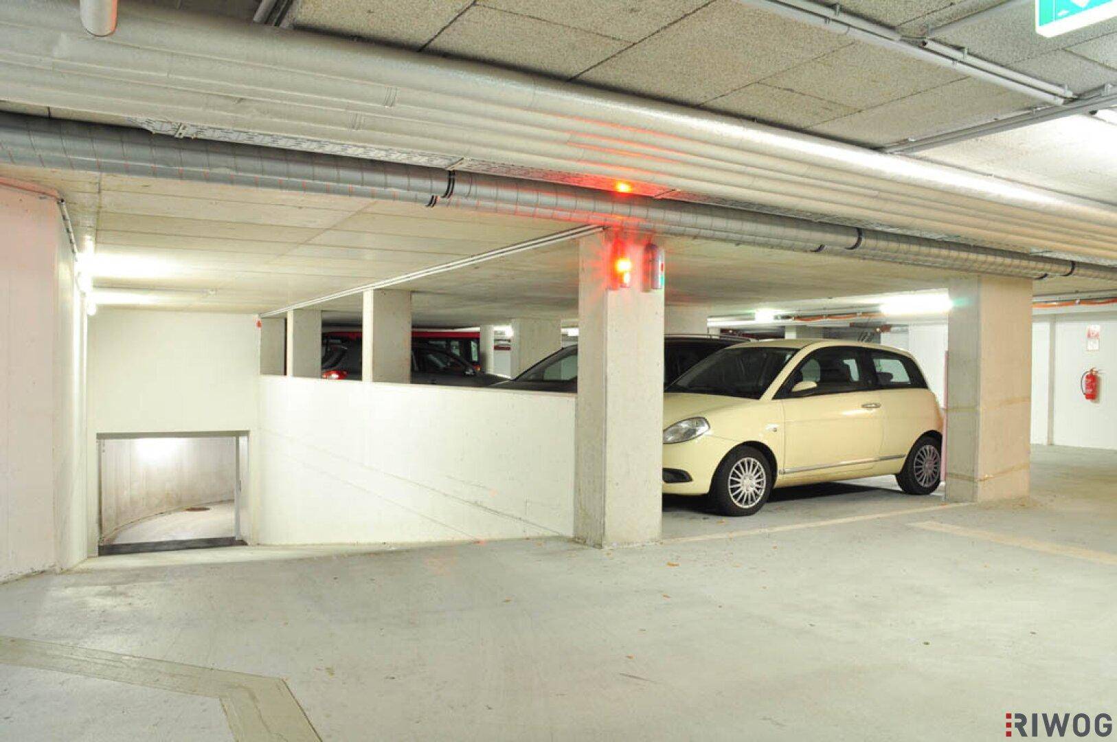 Tiefgarage mit geparkten Fahrzeugen, Betonstützen und einer Rampe im Hintergrund.