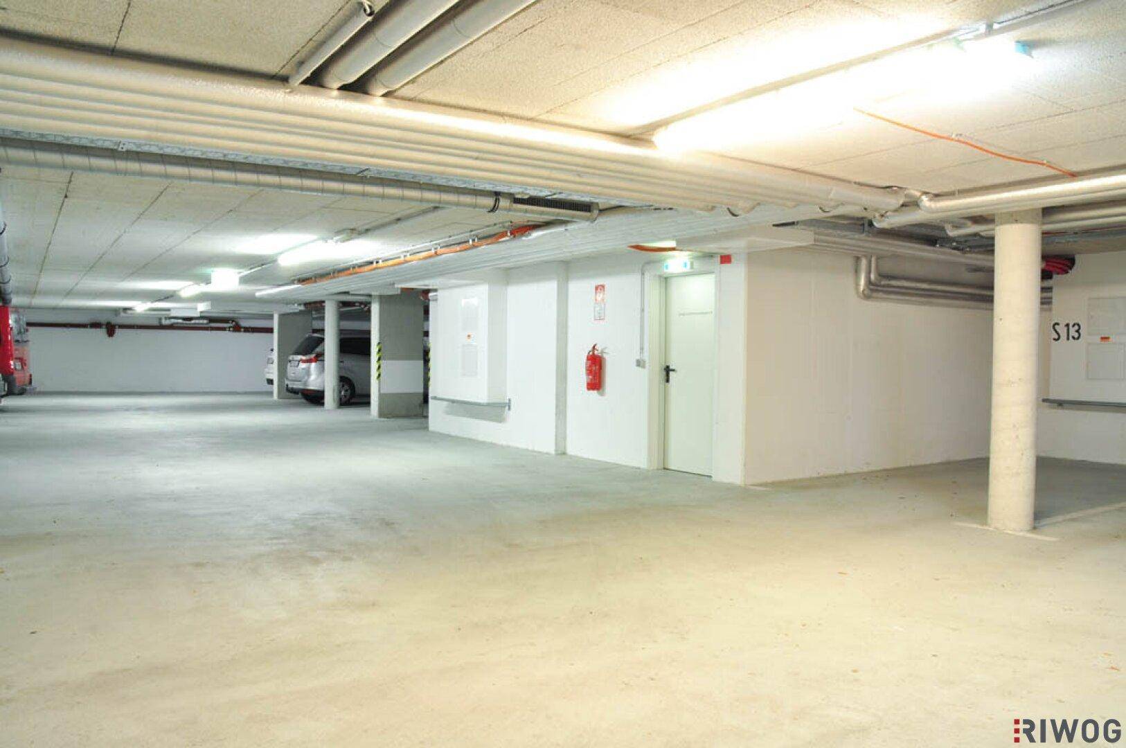 Weitläufige Tiefgarage mit Betonboden, Brandschutzanlage und Zugangstüren zu weiteren Bereichen.