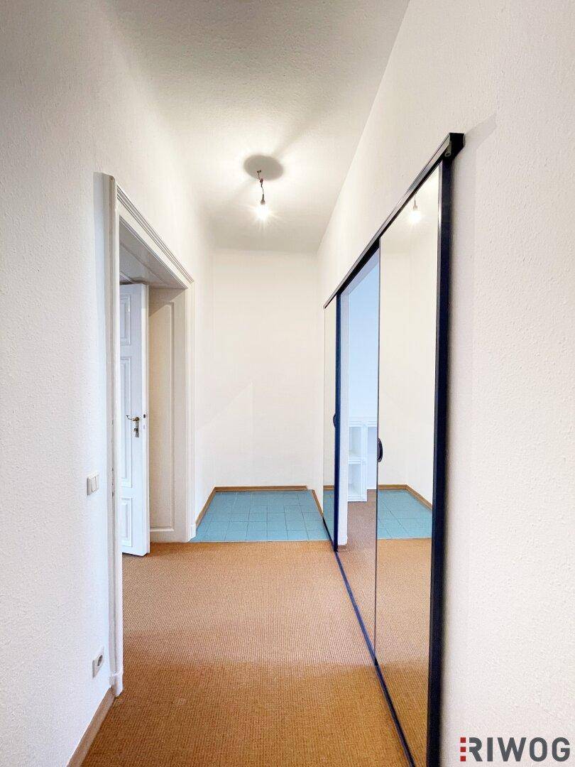 Langer Flur mit Spiegelschiebetür und Übergang zu einem Bereich mit blauen Fliesen.