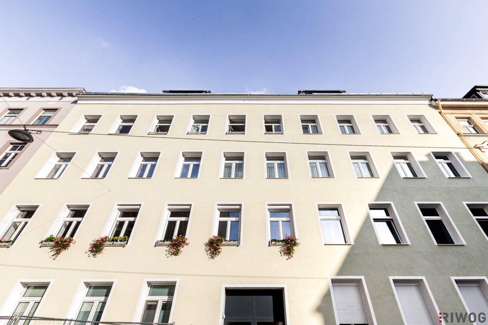Fassade eines Mehrfamilienhauses mit vielen Fenstern und Blumenkästen.