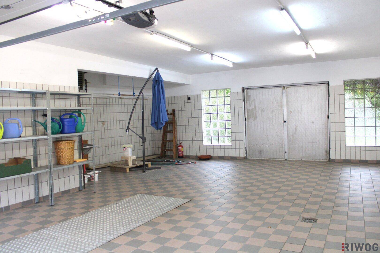 Weiterer Blick in die große Garage mit gefliesten Wänden, Regalen und viel Stauraum für Werkzeuge und Geräte.