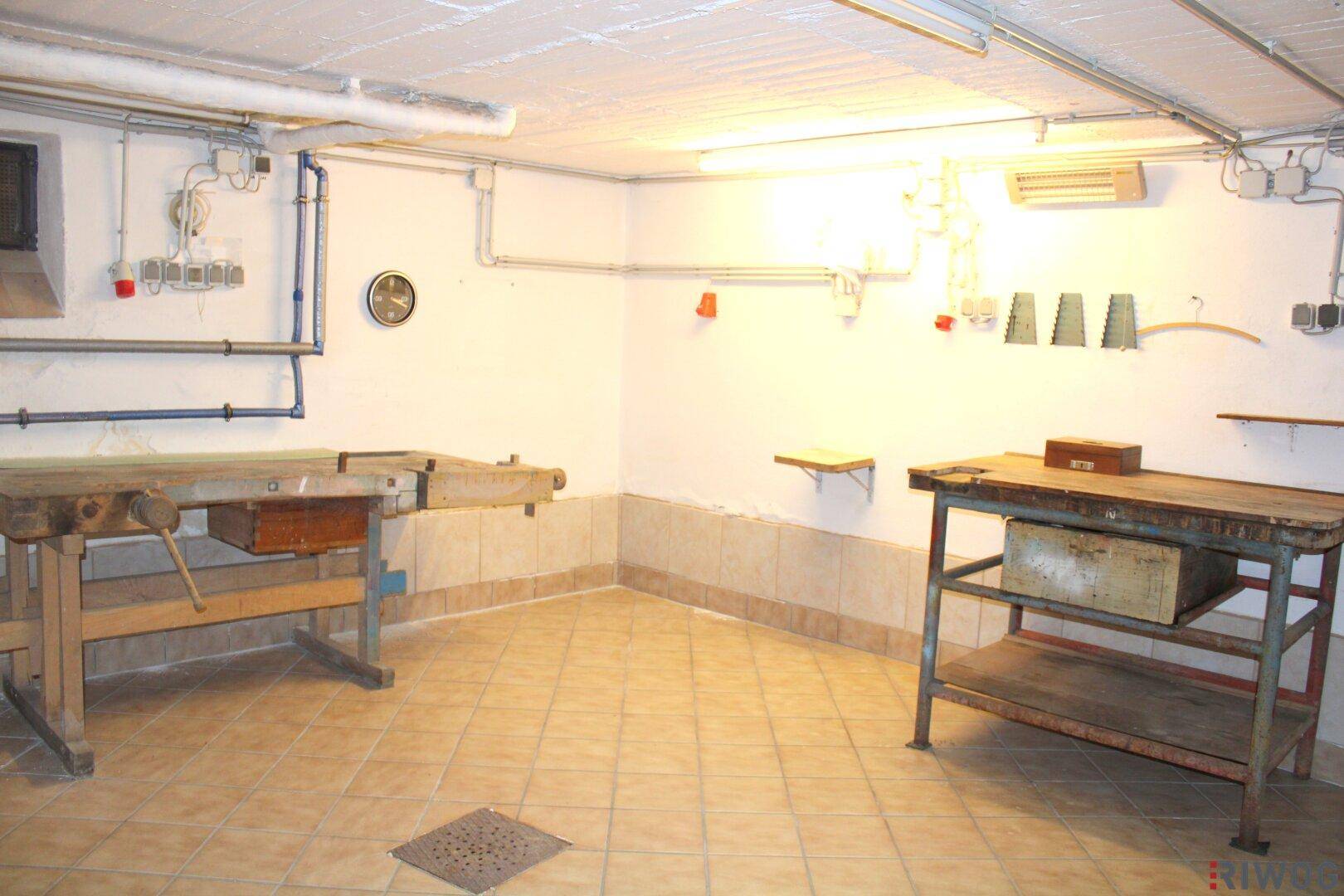 Werkstatt im Keller mit zwei Werkbänken und gefliestem Boden, ideal für handwerkliche Arbeiten und Lagerung.