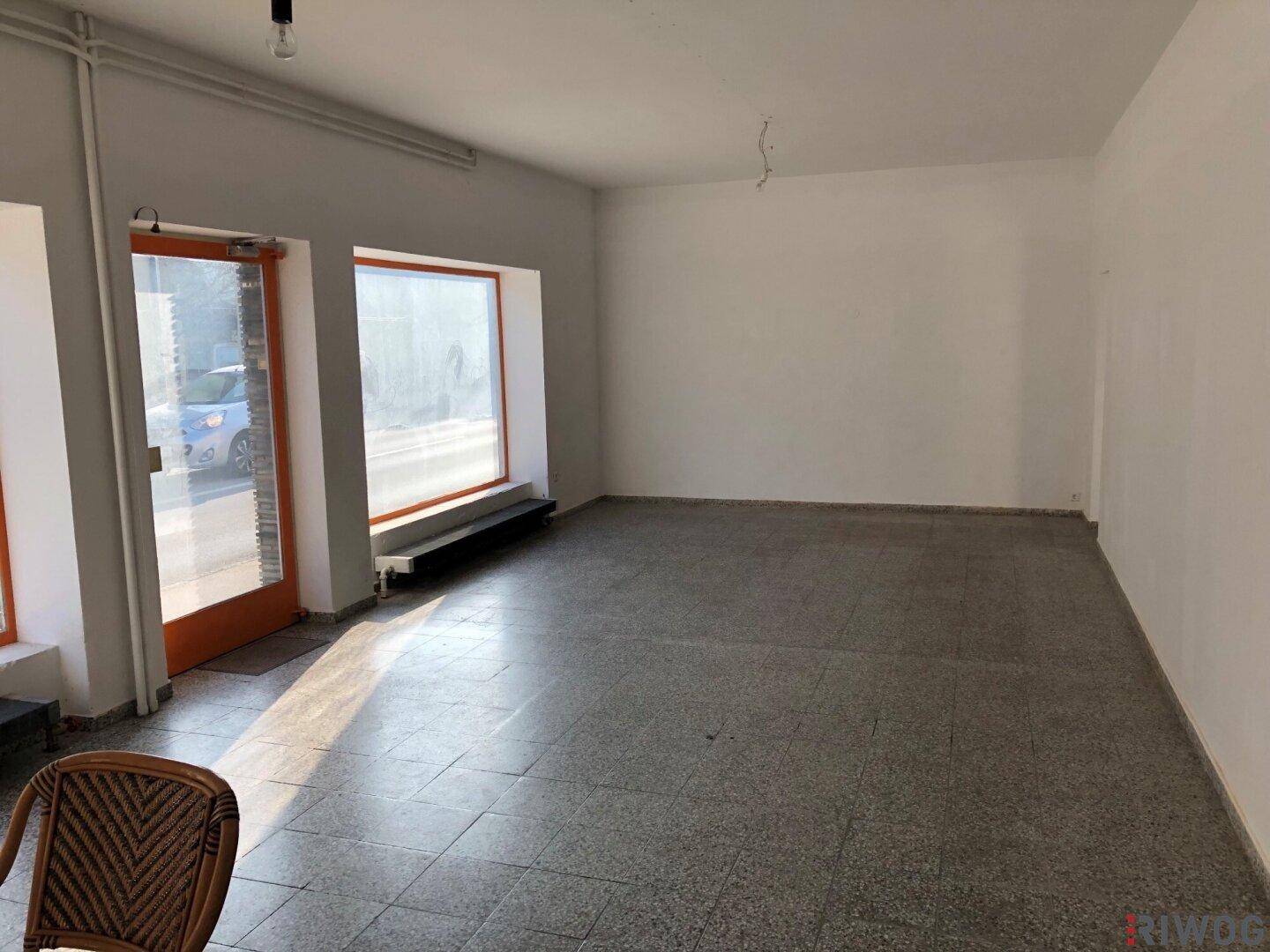 Weiterer Blick in den leeren Geschäftsraum mit großen Schaufenstern und gefliestem Boden.