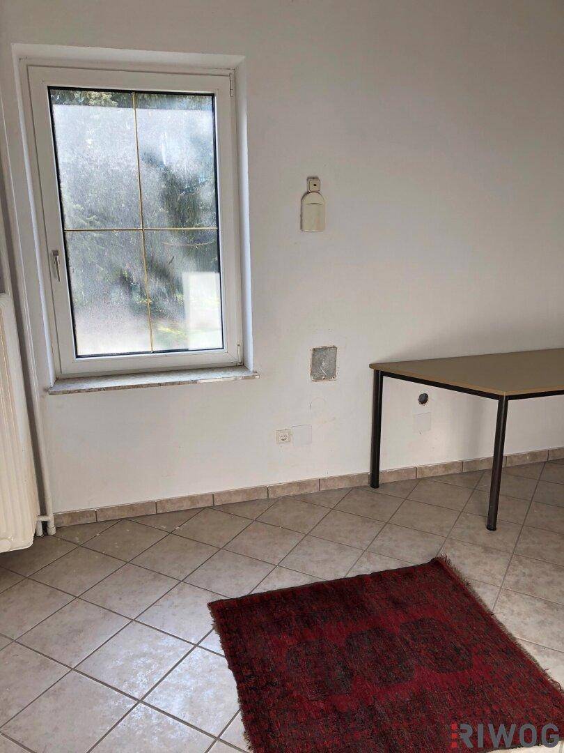 Heller Raum mit Fliesenboden, einem Fenster und einem einfachen Tisch.