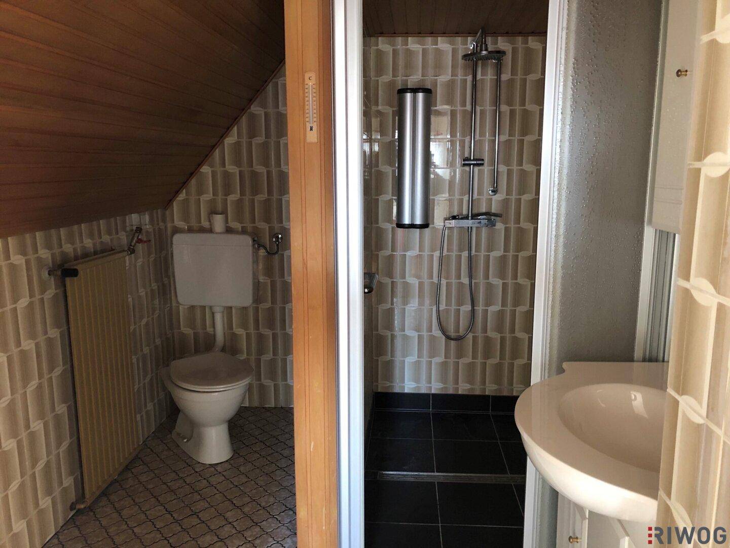 Badezimmer im Dachgeschoss mit Dusche, WC und Waschbecken, gefliest in Braun- und Beigetönen.