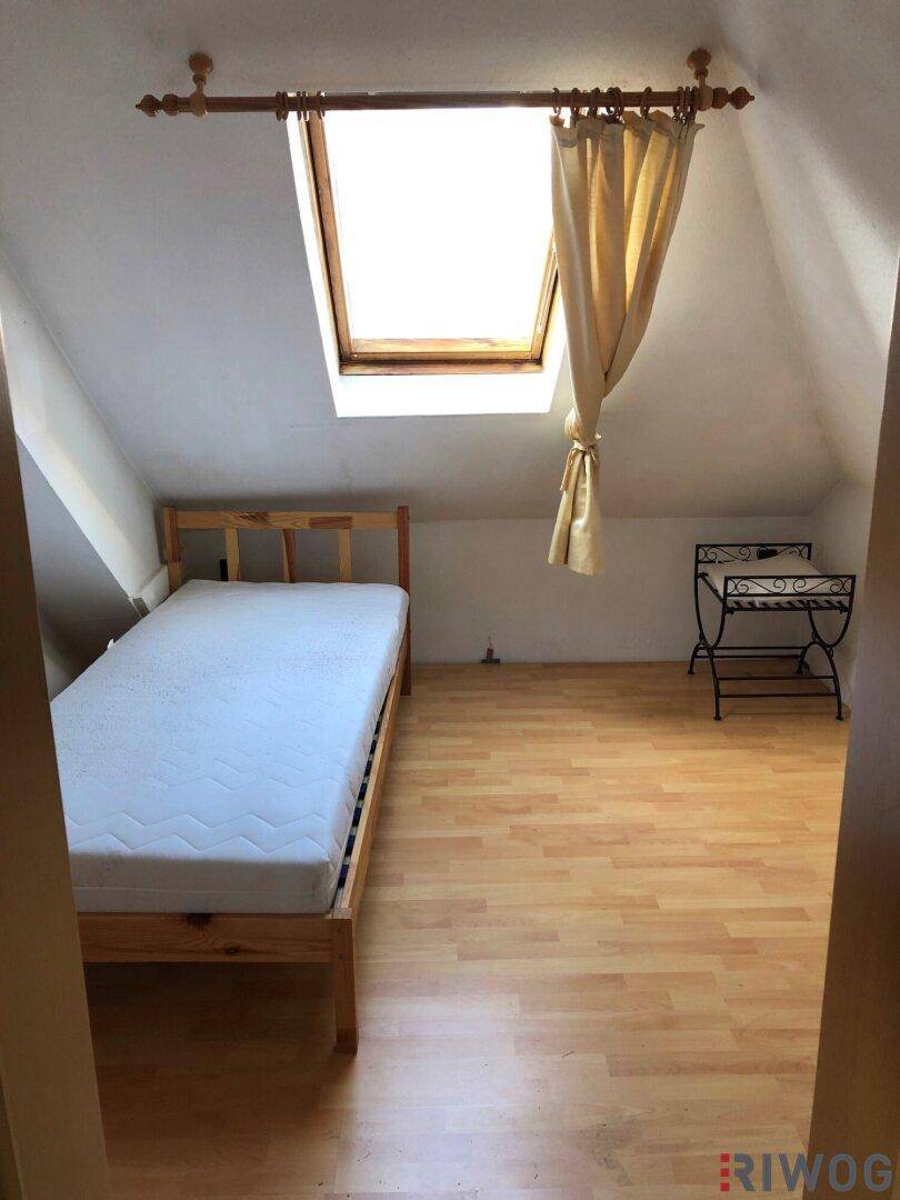 Helles Schlafzimmer im Dachgeschoss mit Holzbett, Parkettboden und Dachfenster.