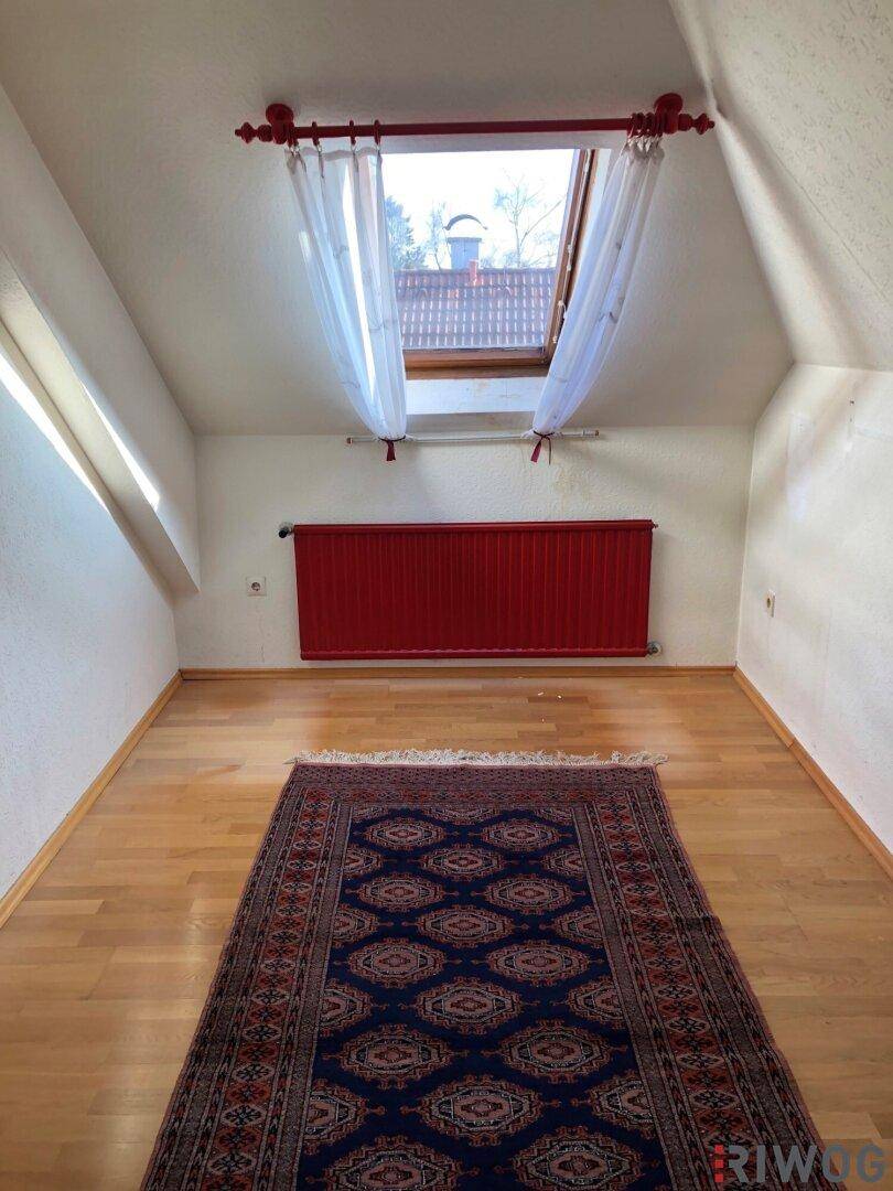 Dachgeschossraum mit rotem Heizkörper, Dachfenster und Parkettboden.