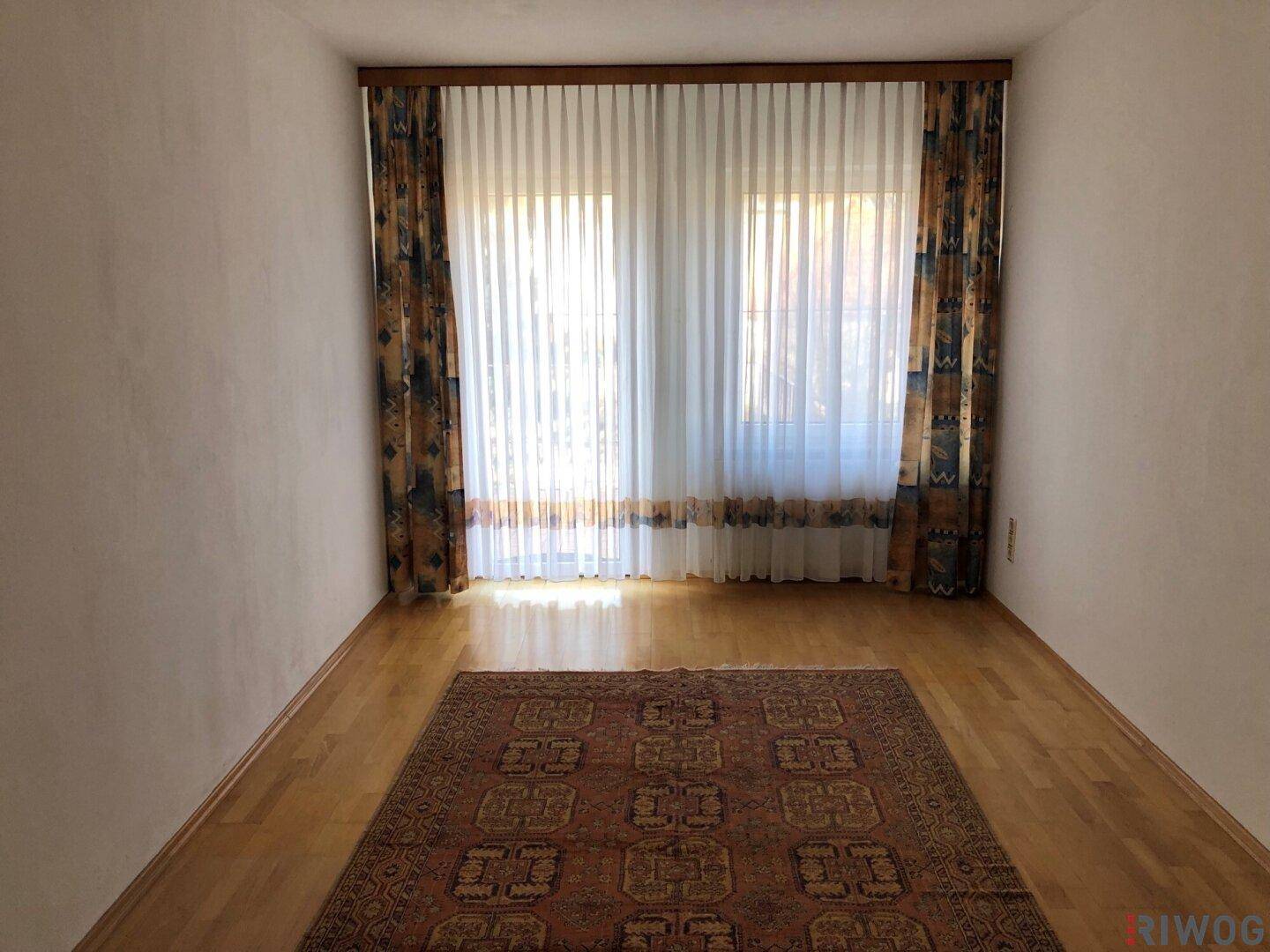 Gemütlicher Raum mit Holzparkett, großen Fenstern und einem traditionellen Teppich.