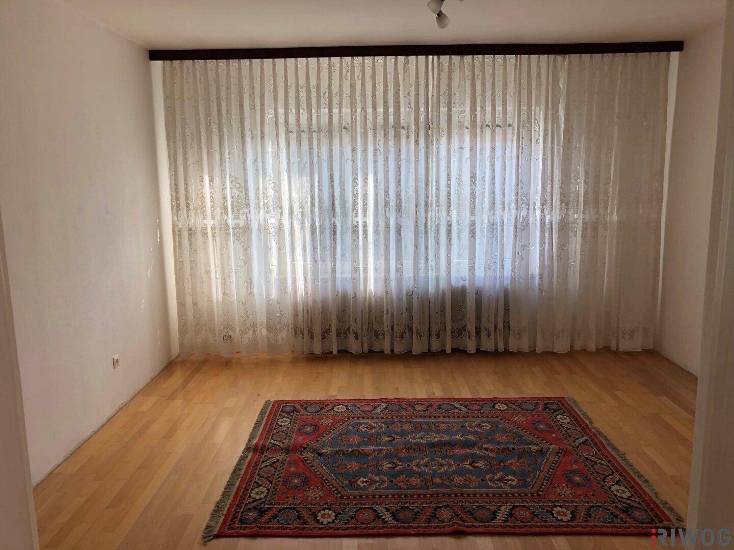 Heller Raum mit Parkettboden und großen Fenstern, die viel Tageslicht hereinlassen.