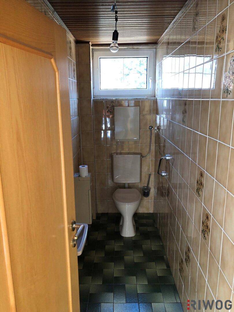 Kleines WC mit Fenster, Toilette und Fliesen in warmen Brauntönen.