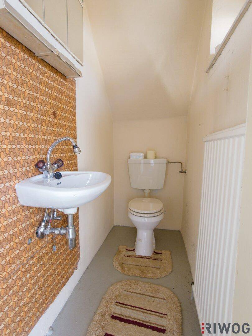 Kleines Gäste-WC mit Waschbecken und Toilette, ausgestattet mit älteren Fliesen.