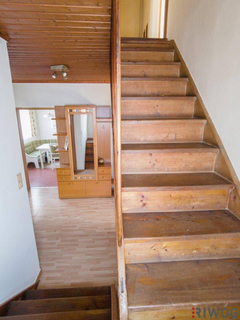 Holztreppe führt in die obere Etage, mit Blick auf den Flur und die Küche.