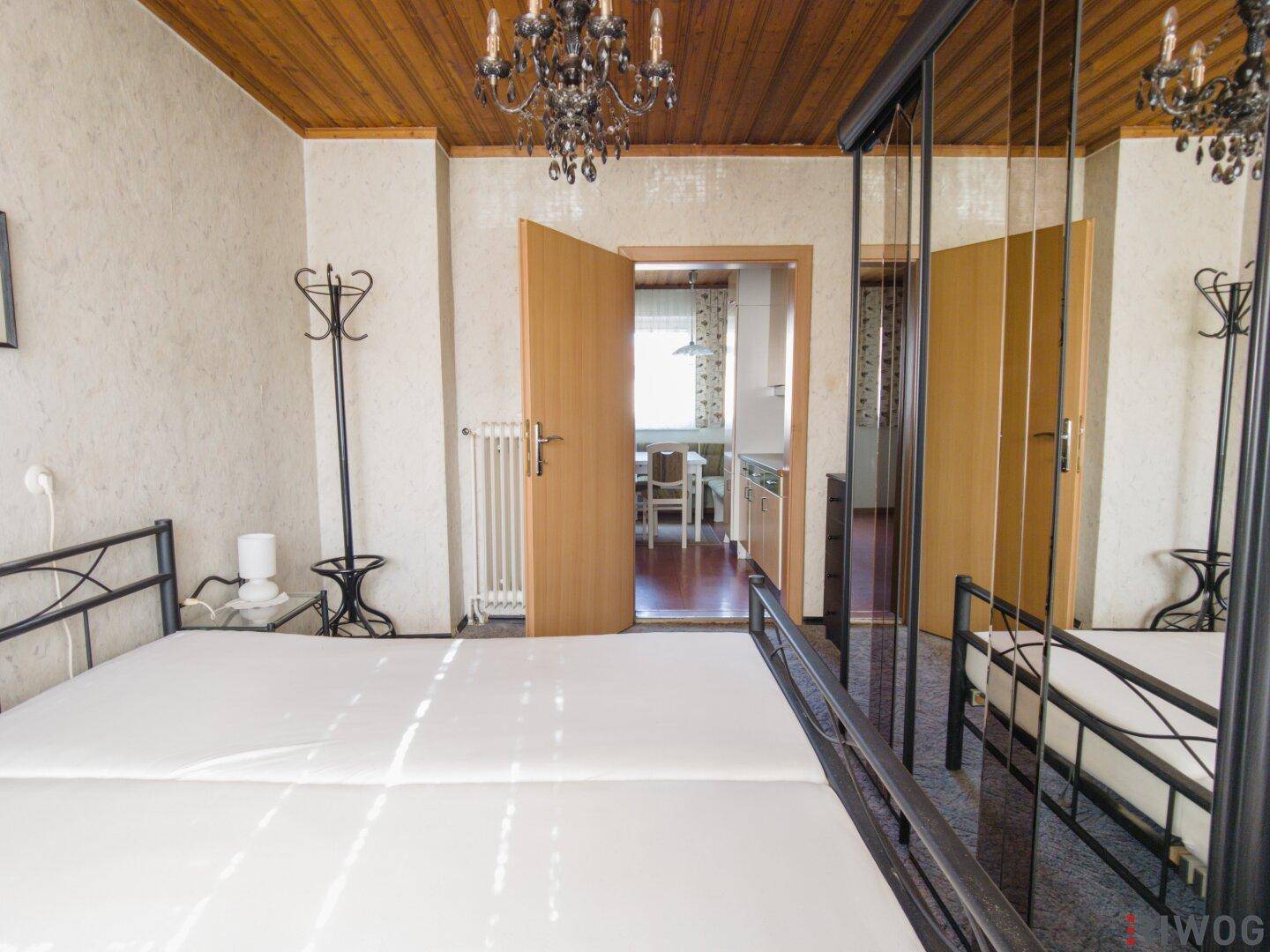 Schlafzimmer mit Doppelbett und Spiegelschrank, bietet Zugang zur Küche und weiteren Räumen.