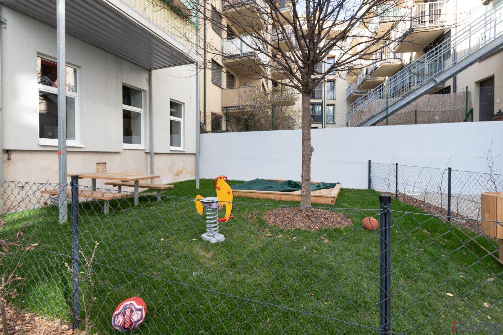 Kleiner Spielplatz mit Rasen, Sandkasten und Schaukelpferd, ideal für Kinder im Freien.