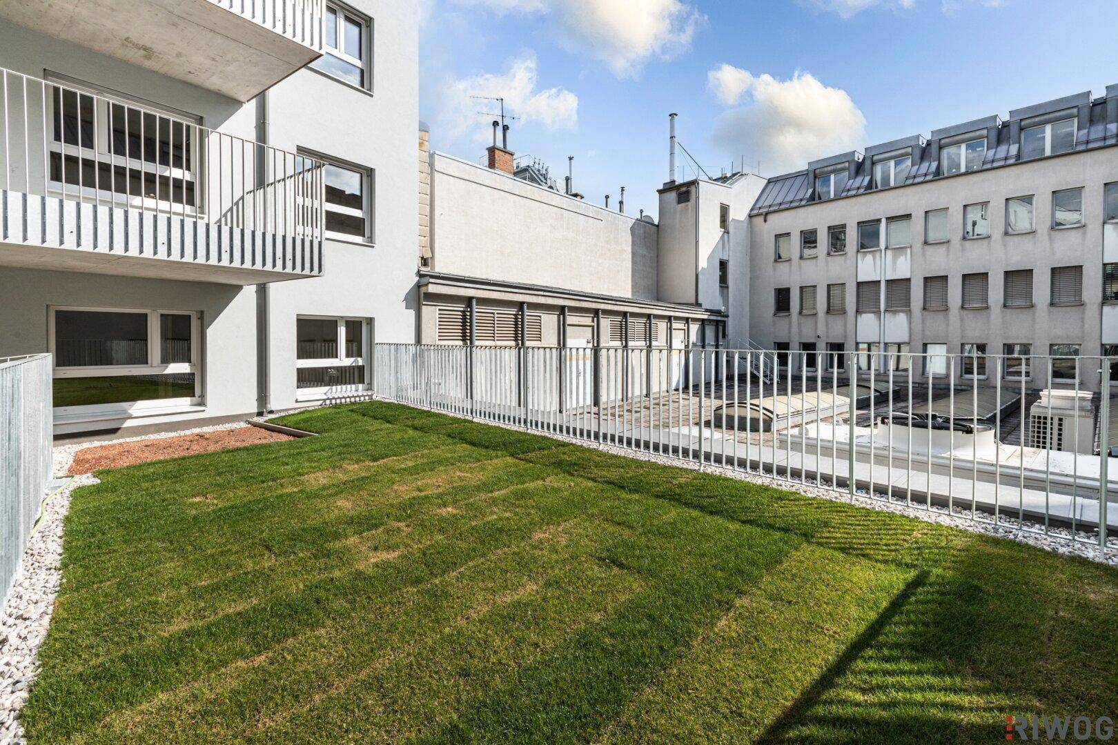 Grüner Gartenbereich mit Rasenfläche und Kiesumrandung neben dem modernen Wohngebäude.