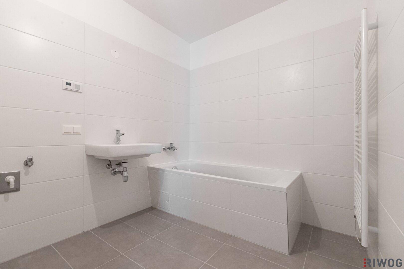 Modernes Badezimmer mit weißen Fliesen, Badewanne, Einzelwaschbecken und Handtuchheizkörper.