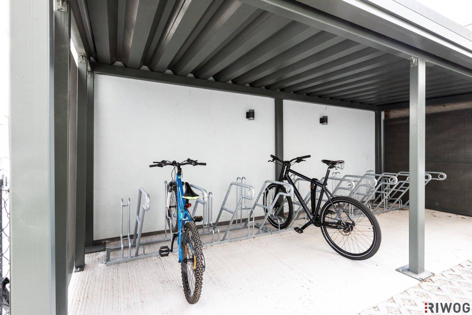 Überdachter Fahrradabstellplatz mit Fahrradständern und zwei Fahrrädern, bietet Schutz vor Witterung.