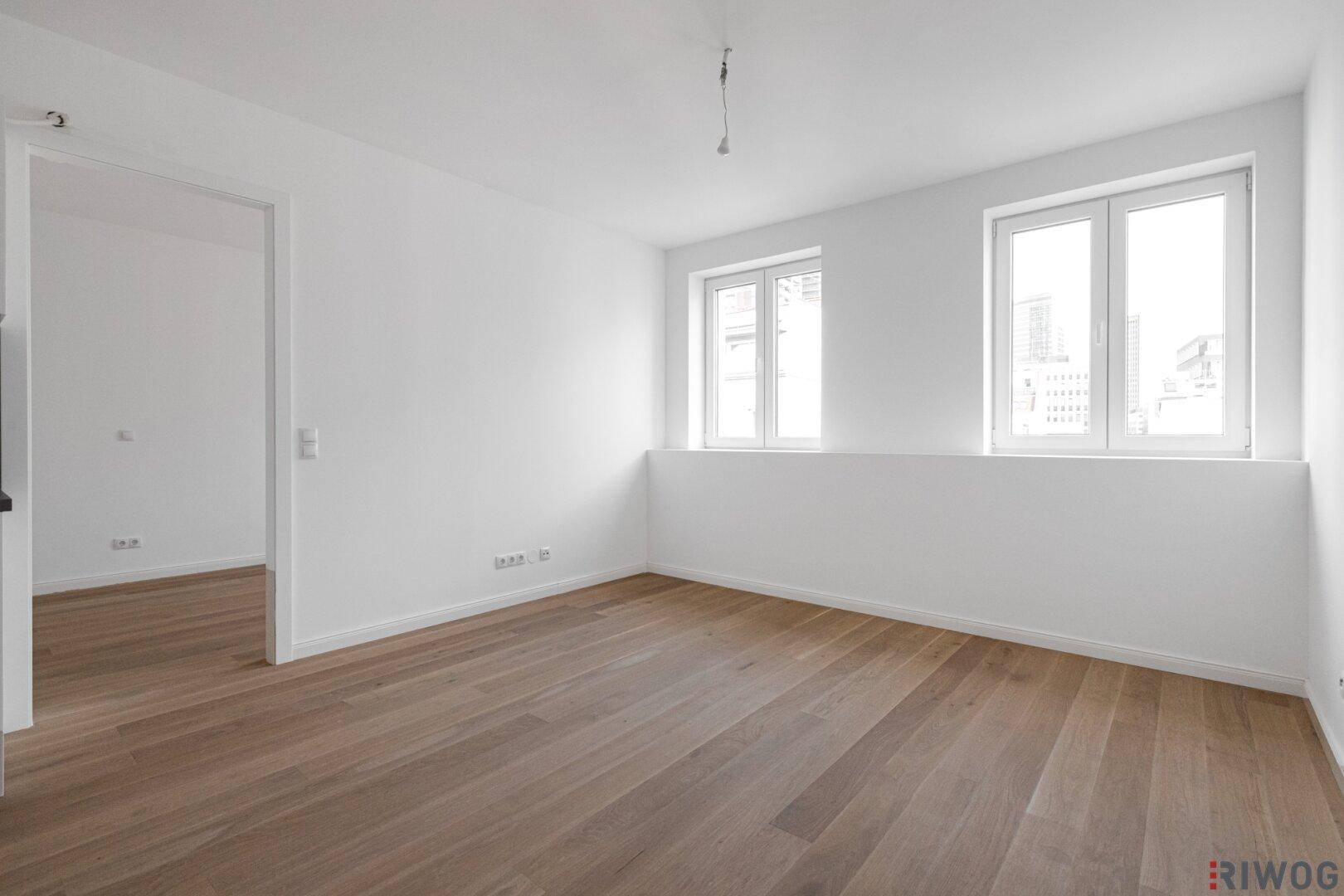 Heller Wohnraum mit großen Fenstern und neuem Parkettboden, bereit zur individuellen Gestaltung.