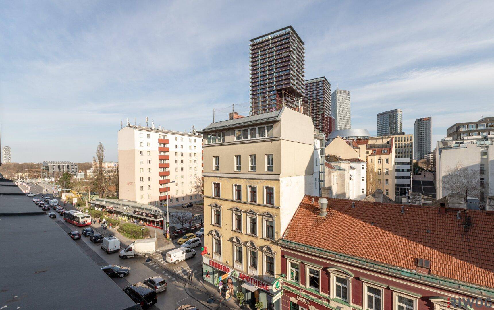 Weitläufiger Stadtblick über Dächer und Straßen mit modernen Hochhäusern im Hintergrund.