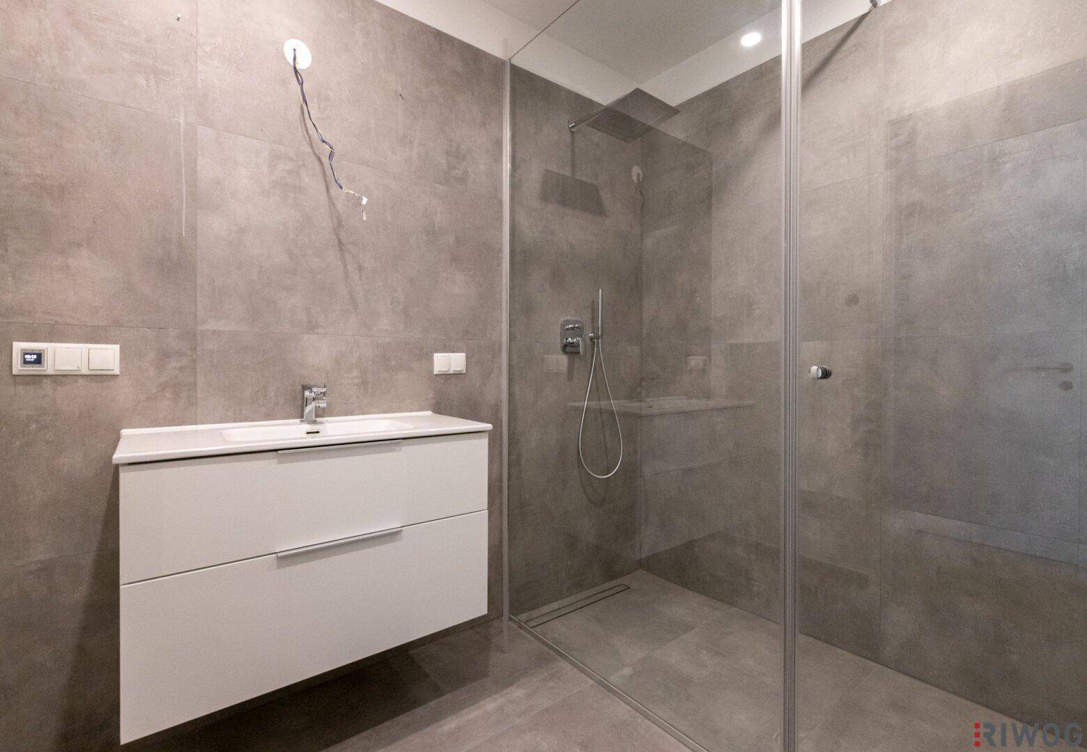 Modernes Badezimmer mit großformatigen grauen Fliesen, Einzelwaschbecken und ebenerdiger Dusche.