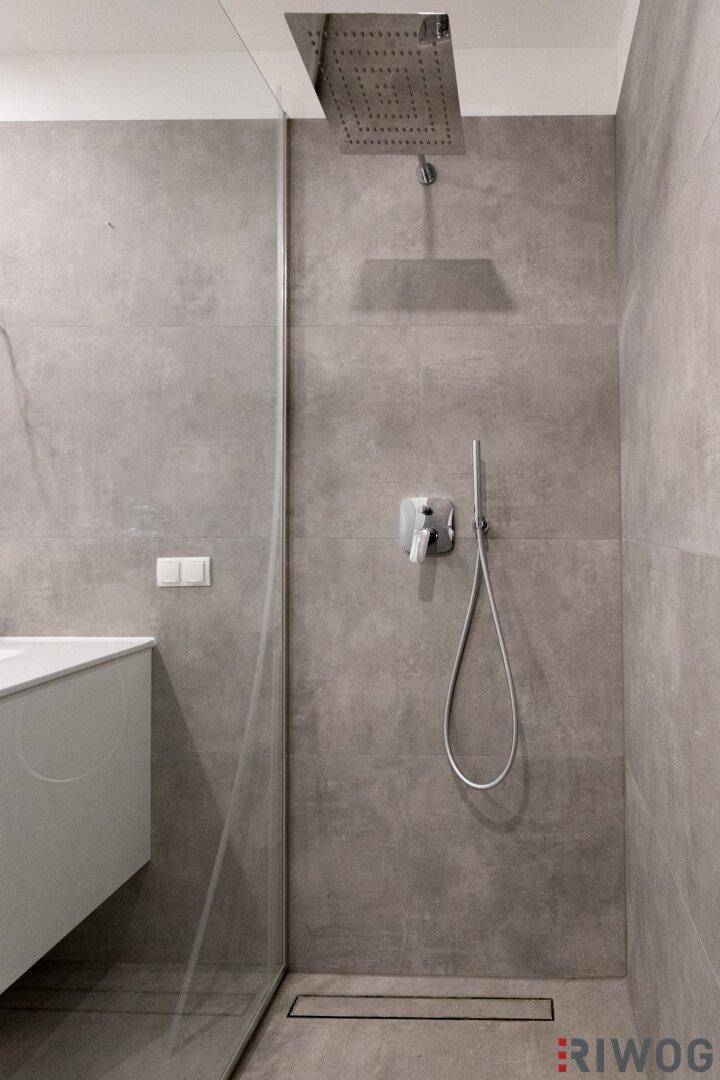 Ebenerdige Dusche mit Regenduschkopf und modernen grauen Fliesen im Badezimmer.