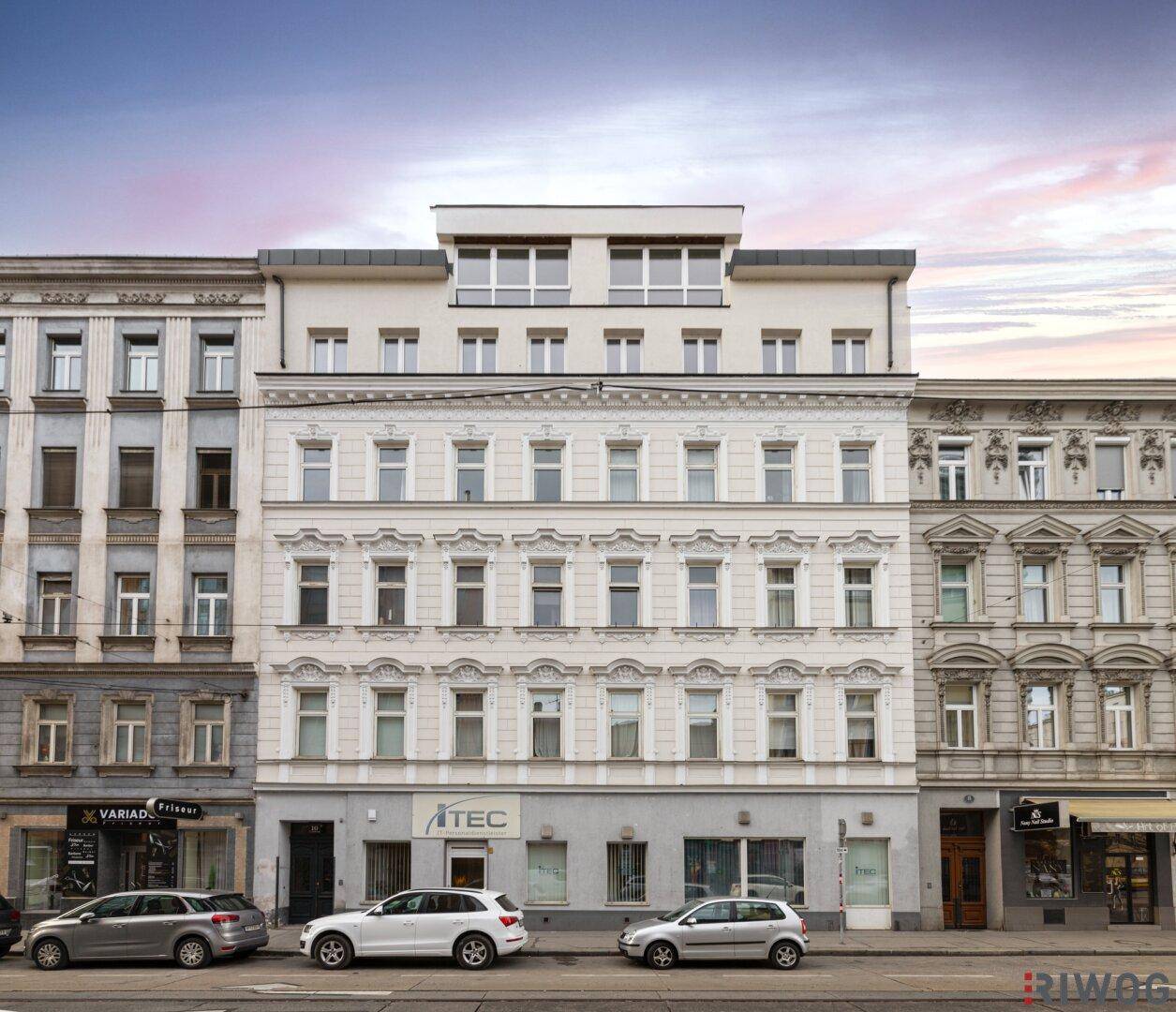 Historische Fassade eines Altbaus mit modernem Dachausbau und Geschäften im Erdgeschoss.