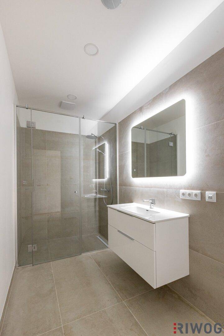 Modernes Badezimmer mit begehbarer Dusche, großformatigen Fliesen, schwebendem Waschtisch und beleuchtetem Spiegel.