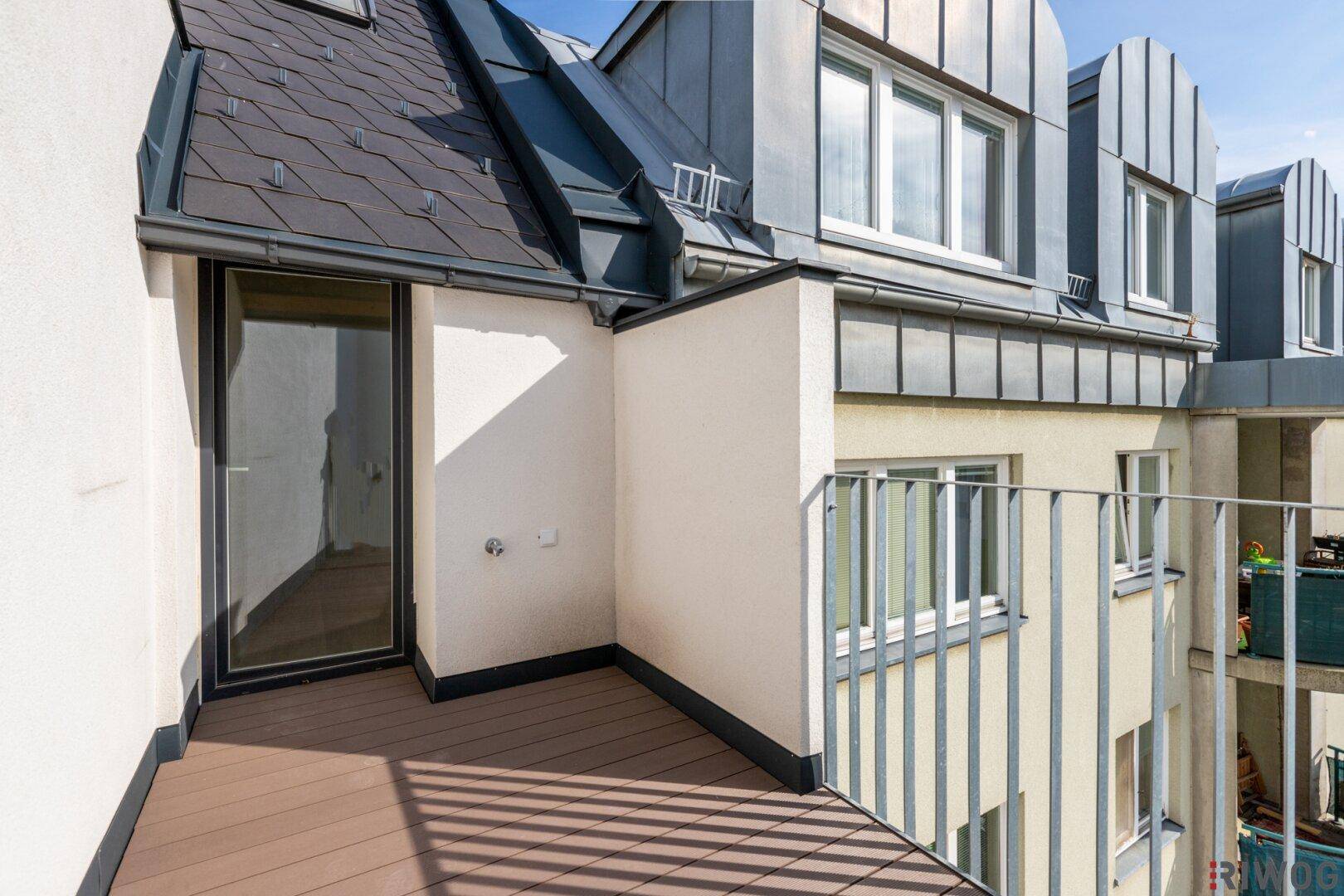 Kleiner, moderner Balkon mit Holzboden und Blick auf die umliegenden Dächer und Gebäude.