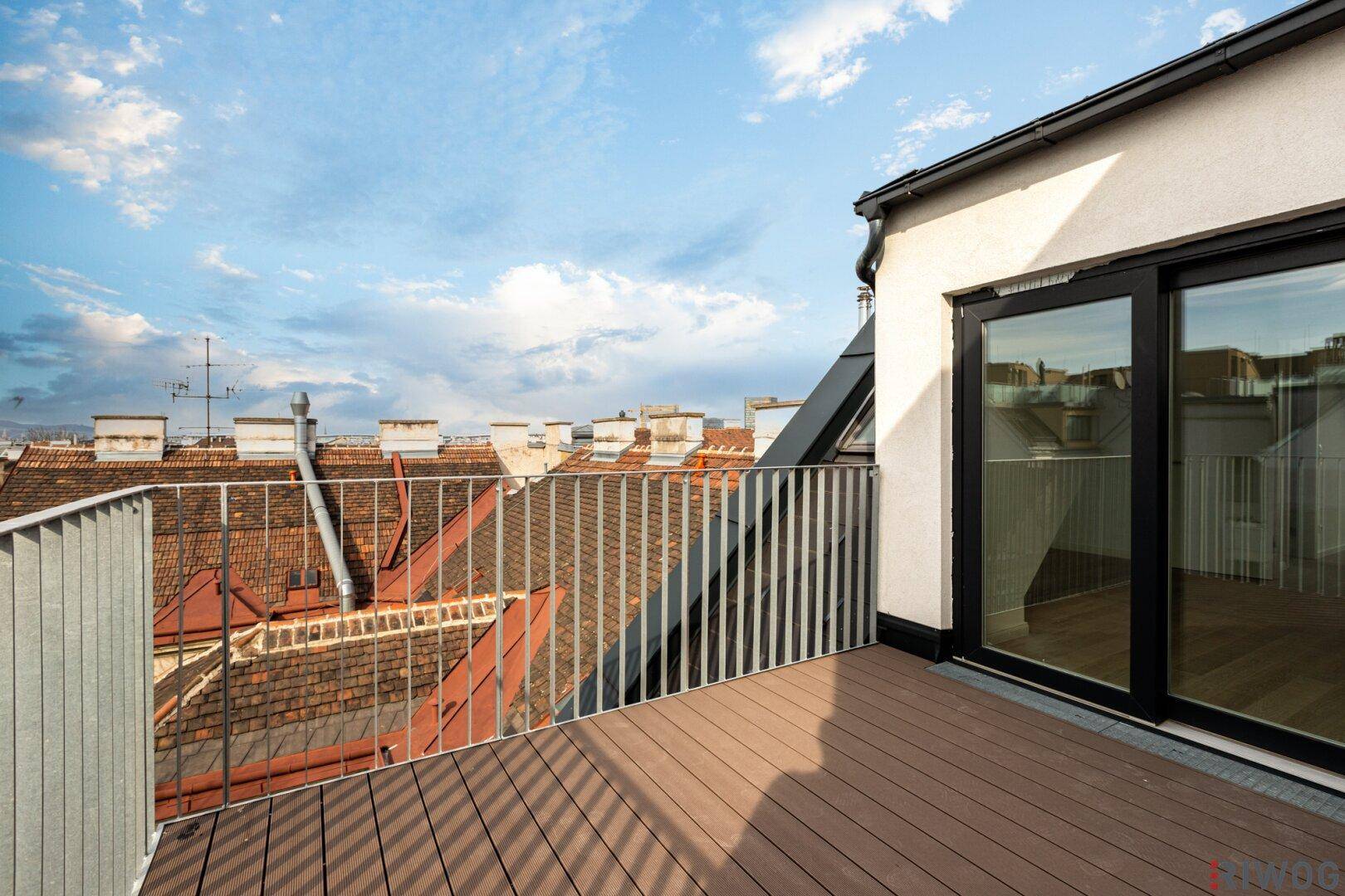 Geräumiger Balkon mit Holzboden und Panoramablick über die Dächer der Stadt und den Himmel.