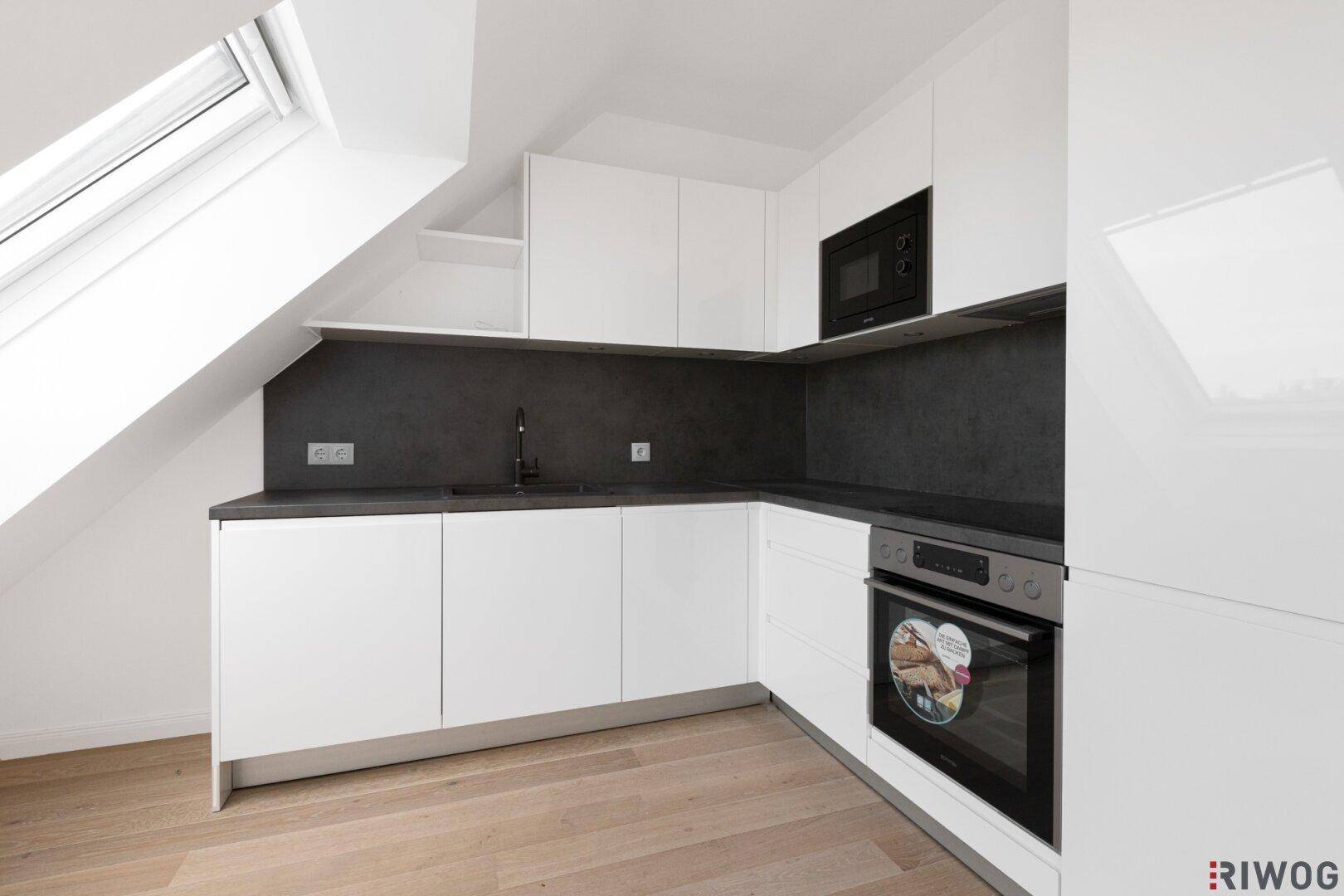 Moderne Einbauküche im Dachgeschoss mit weißen Hochglanzfronten und dunkler Arbeitsplatte.