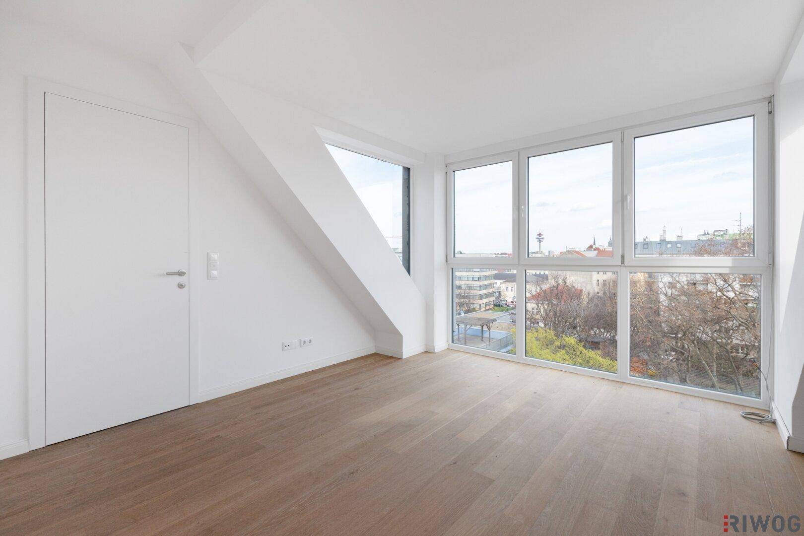 Geräumiger Dachgeschossraum mit schrägen Wänden, Holzboden und großen Fenstern.