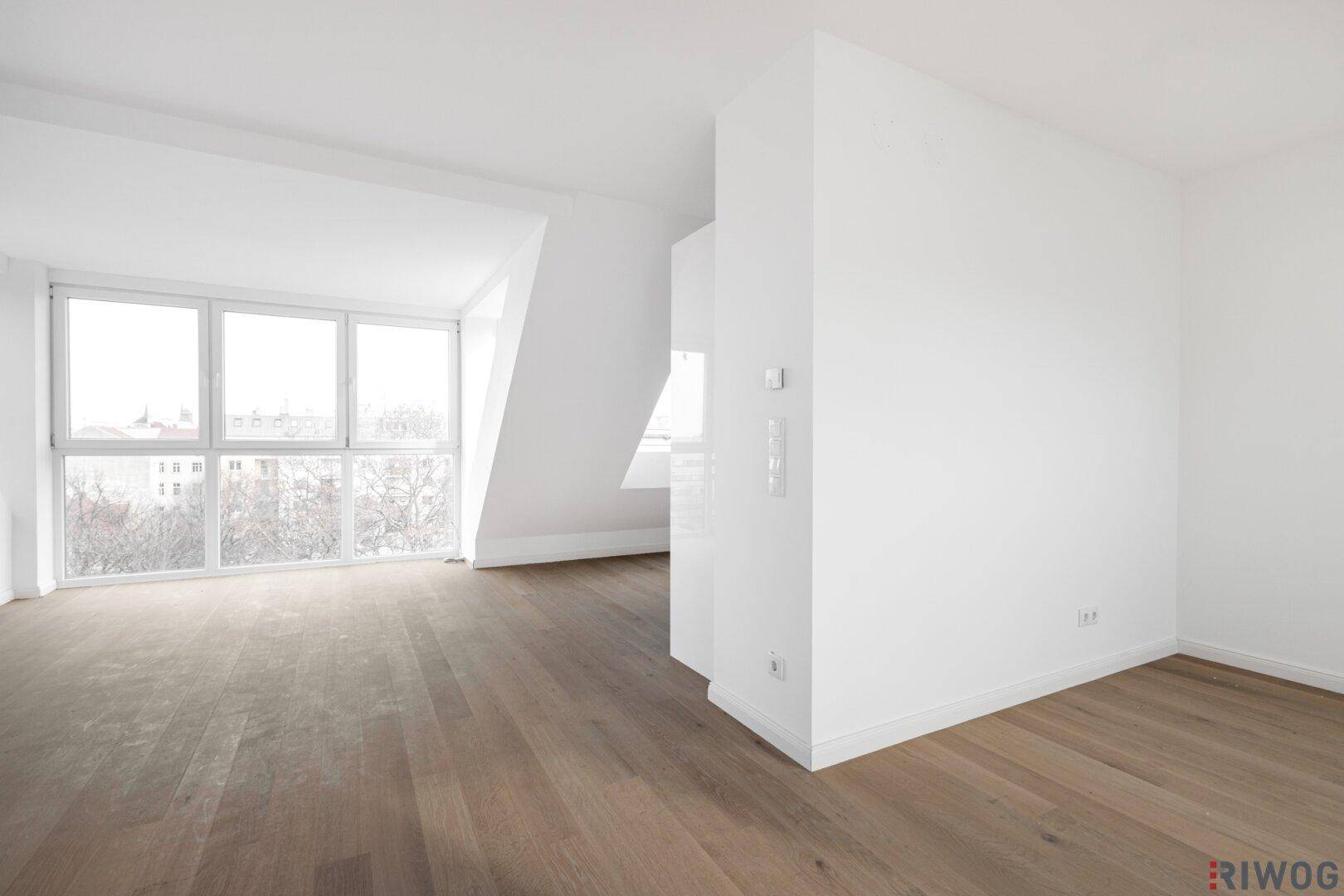 Heller Dachgeschossraum mit Holzboden, schrägen Wänden und großen Fenstern.